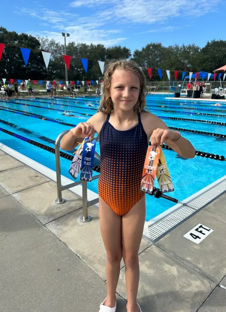 BCS swim team student holding up multiple place ribbons at an outdoor swim meet