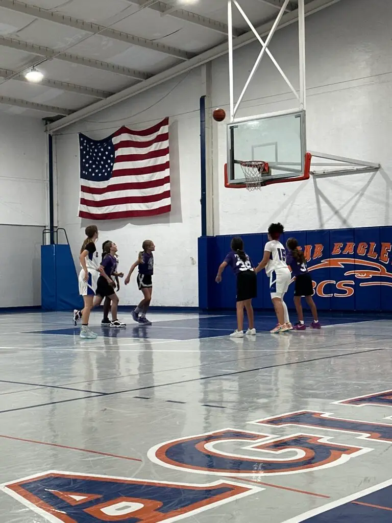 BCS girls basketball team mid-game shooting a basket under the American flag