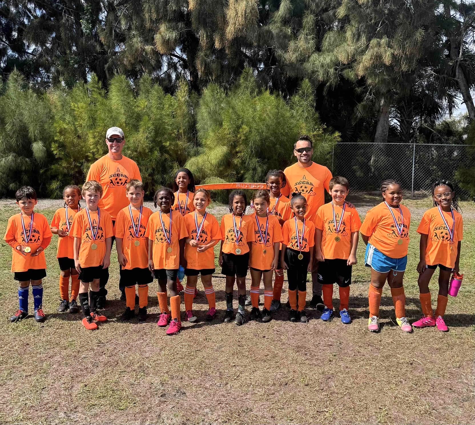 Bethany Christian School Youth Soccer Team with Volunteer Coaches BCS youth soccer team with volunteer coaches posing after a game, wearing bright orange jerseys and medals