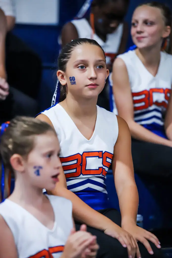 Elementary BCS cheerleaders with face paint watching a game from the sideline